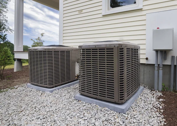 Two residential AC units installed on gravel beside a house